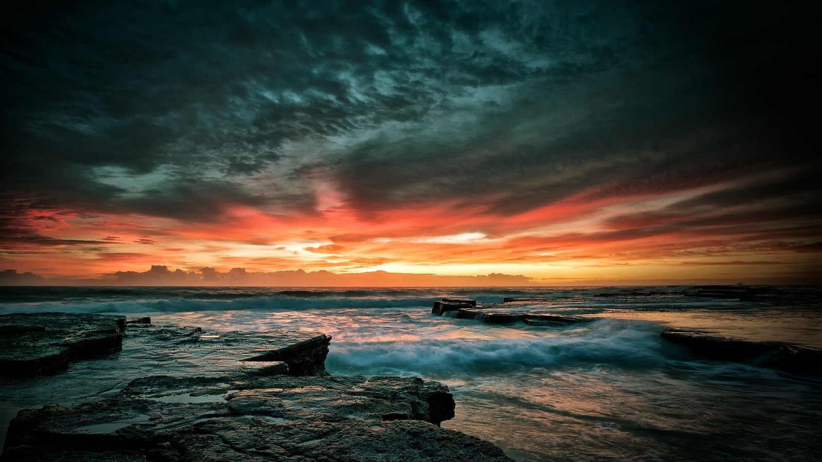 Una vista de una puesta de sol sobre el océano con rocas y olas (paisaje marino, atardecer, horizonte, mar, nubes)