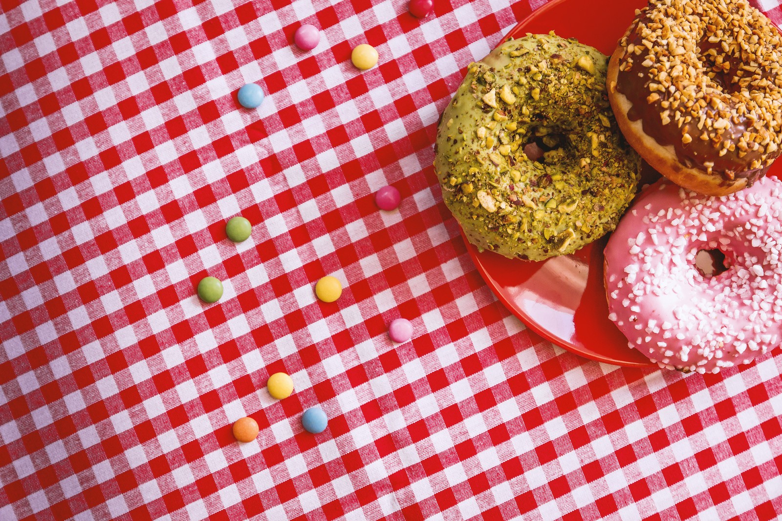 Hay tres donuts en un plato rojo sobre un mantel de cuadros (donut, postre, horneado, comida, cocina)