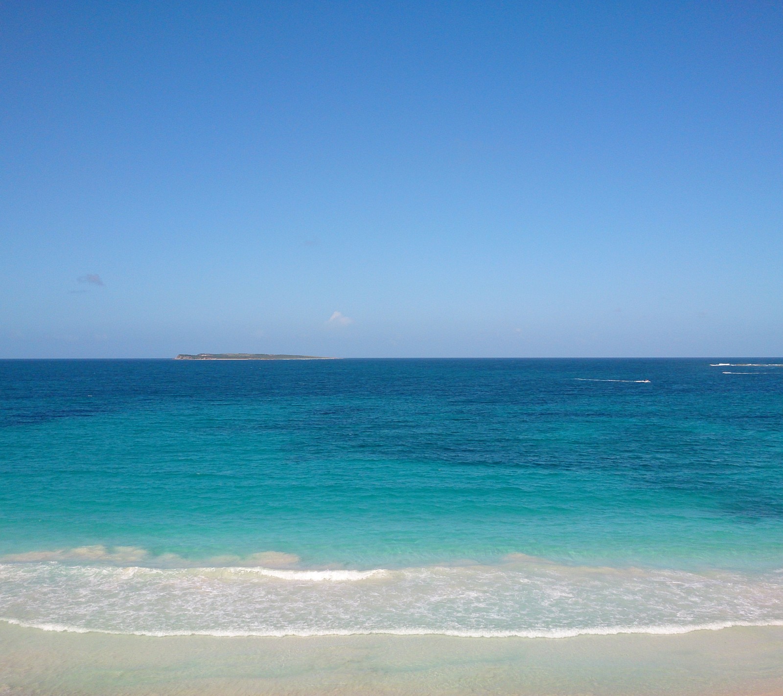 Es gibt einen blick auf einen strand mit einem boot in der ferne. (strand, sand, himmel, sxm, sxm strand)