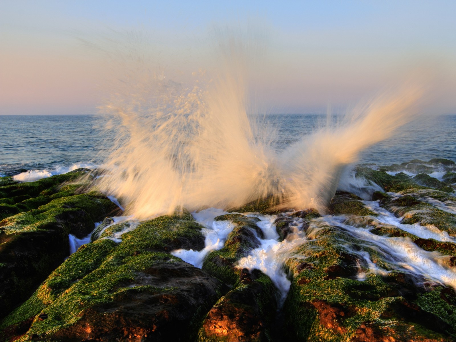 Une vague se brisant sur les rochers sur la plage au coucher du soleil (vague, mer, eau, océan, la côte)