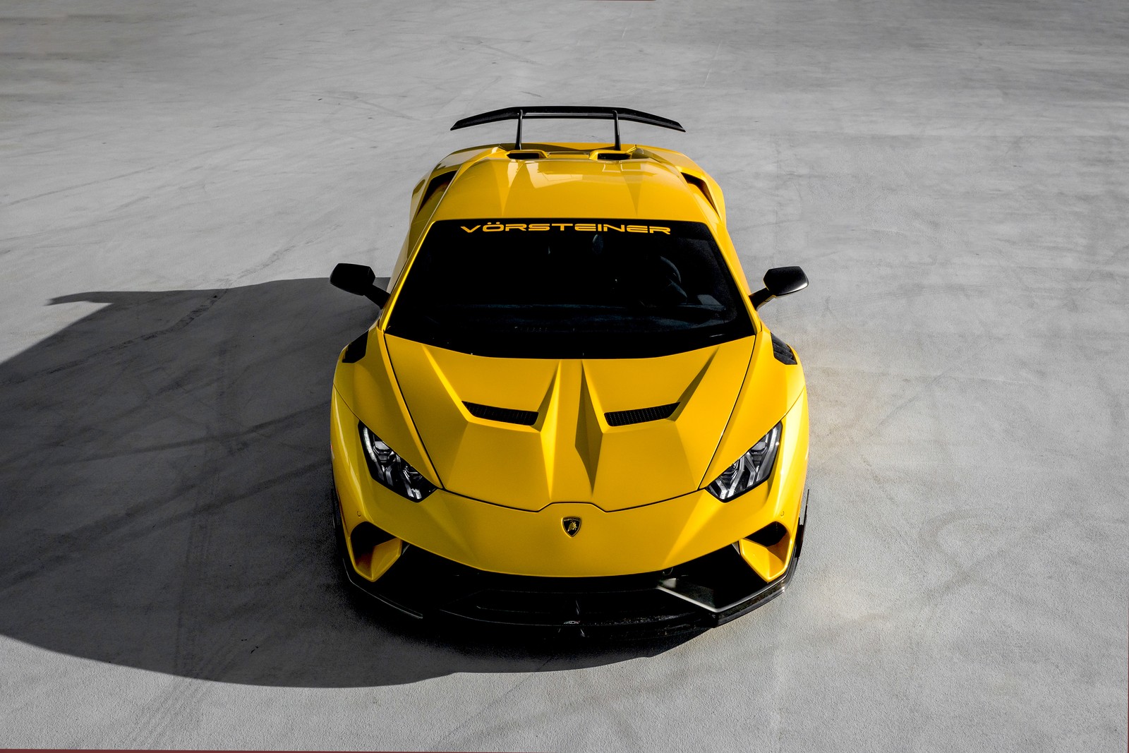 Un primer plano de un coche deportivo amarillo estacionado sobre una superficie de concreto (lamborghini huracán, lamborghini huracan, vorsteiner, coches, fondo de pantalla 4k)