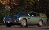 Aston Martin DB5 en vert classique avec des roues à rayons, sur fond naturel.