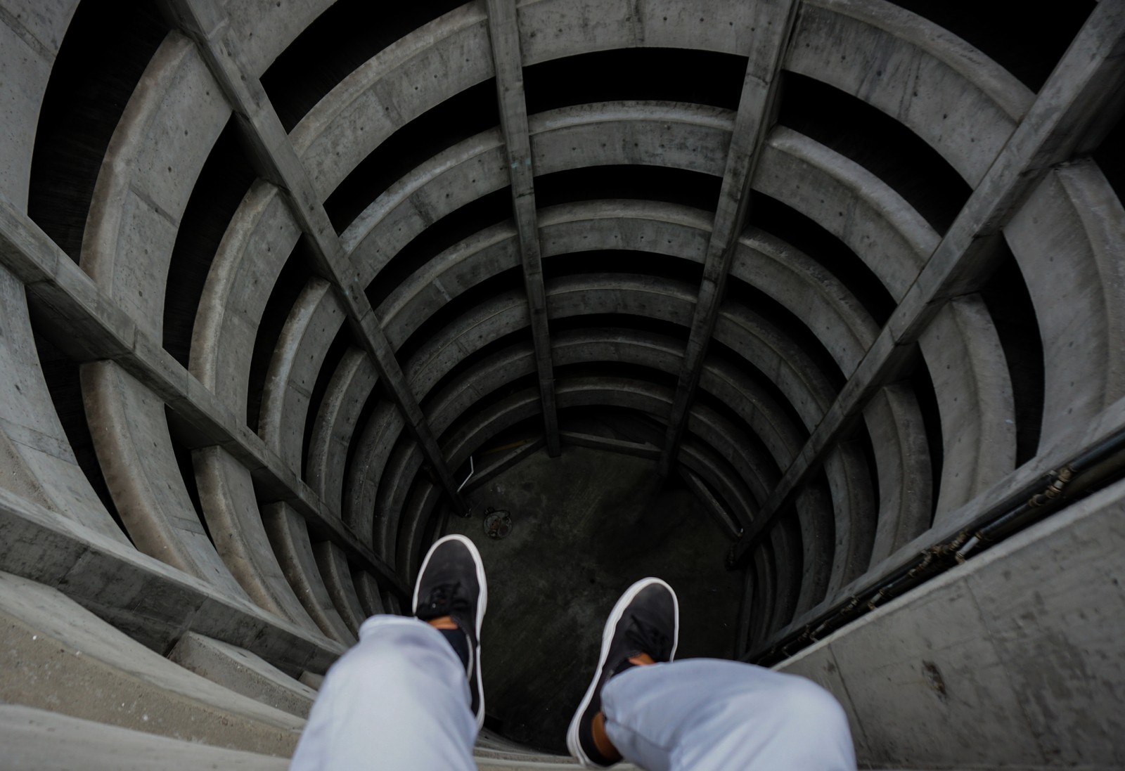 Hay un hombre de pie en un conjunto de escaleras con los pies en el suelo (arquitectura, arco, espiral, escalera, túnel)