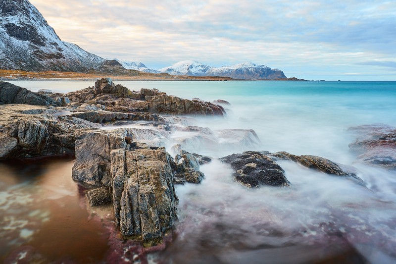 Вид на скалистый пляж с горой на заднем плане (skagsanden beach, утес, камни, океанский синий, вид с небес)