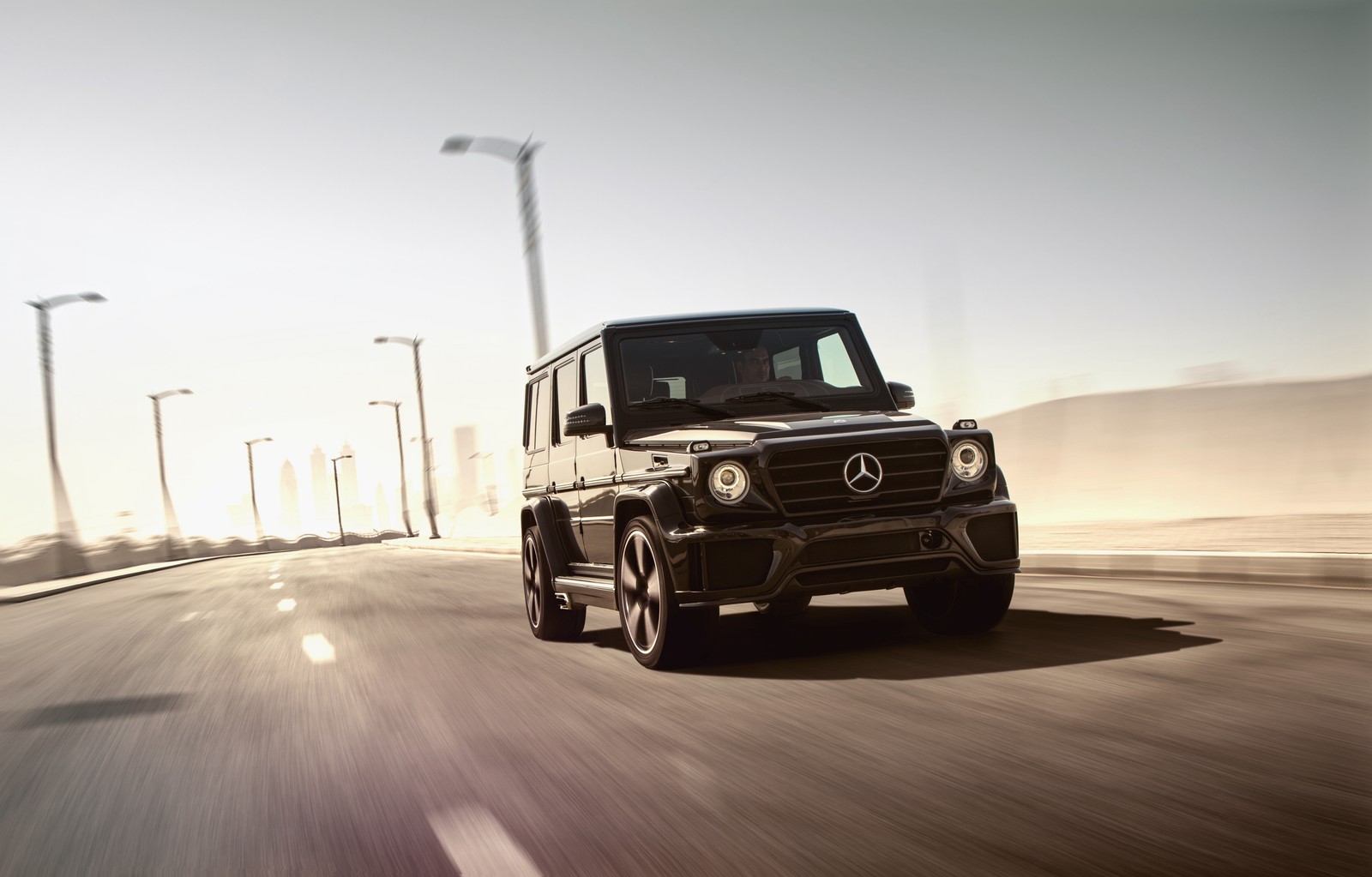 Un primer plano de un mercedes g-class negro conduciendo por una carretera (coche, ajuste de autos, rueda, transporte, mercedes benz g class)