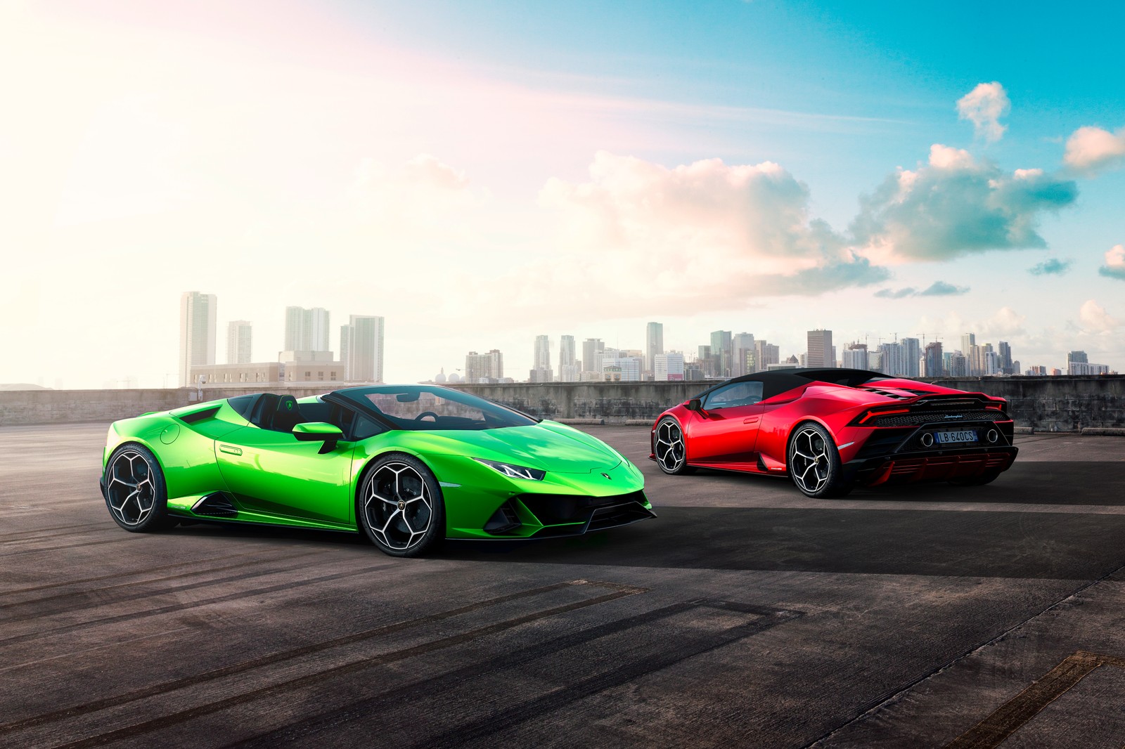 Two lambs parked on a parking lot with a city in the background (lamborghini, sports car, car, supercar, sports car racing)