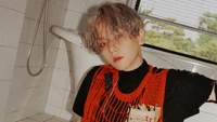 Baekhyun em um top de malha vermelho ousado em um ambiente de banheiro minimalista