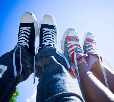 Pareja joven en zapatos Converse contra un cielo brillante