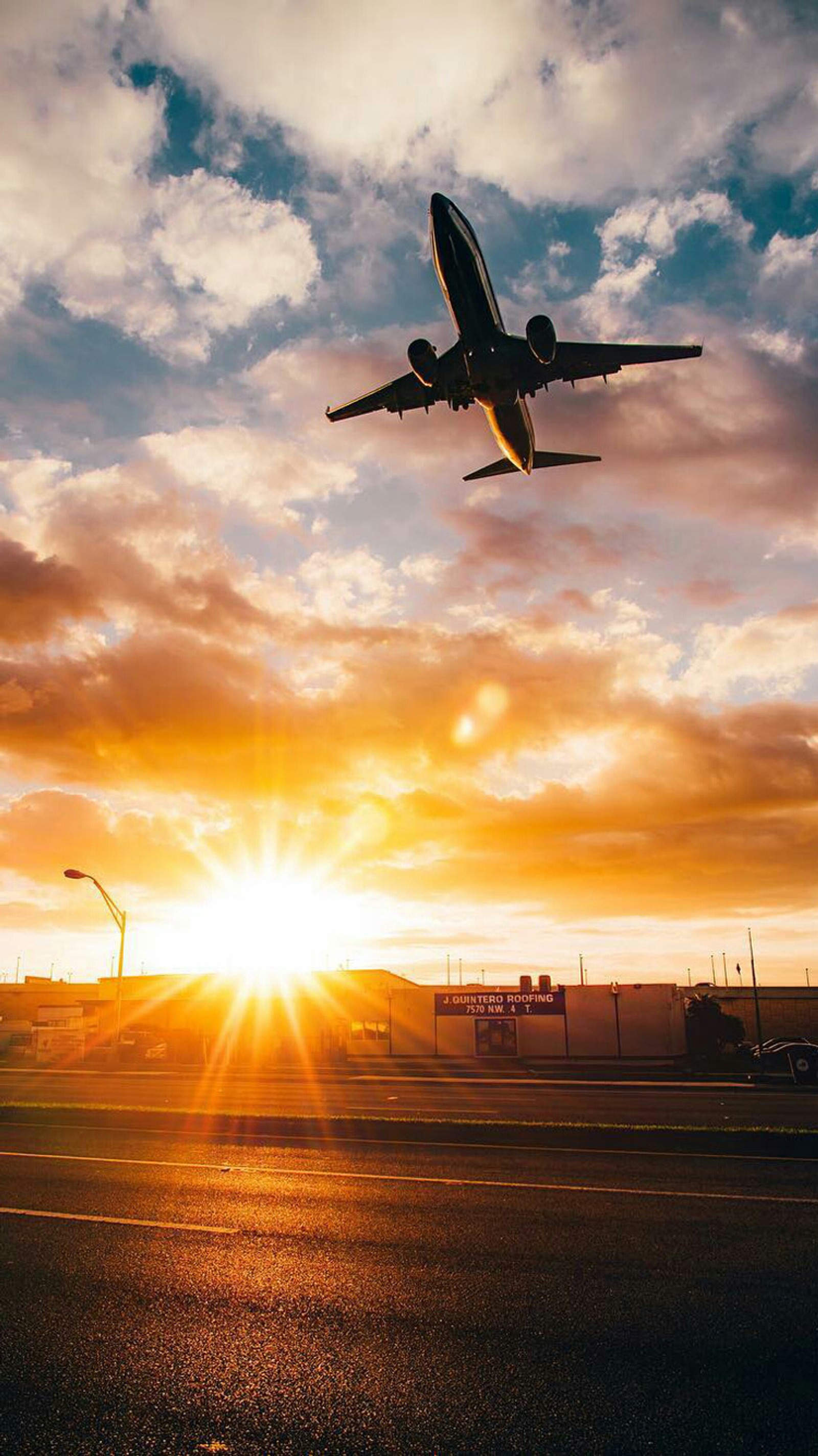 Um avião voando sobre uma pista ao pôr do sol com um edifício ao fundo (aeronave, cidade, voo, voando, miami)