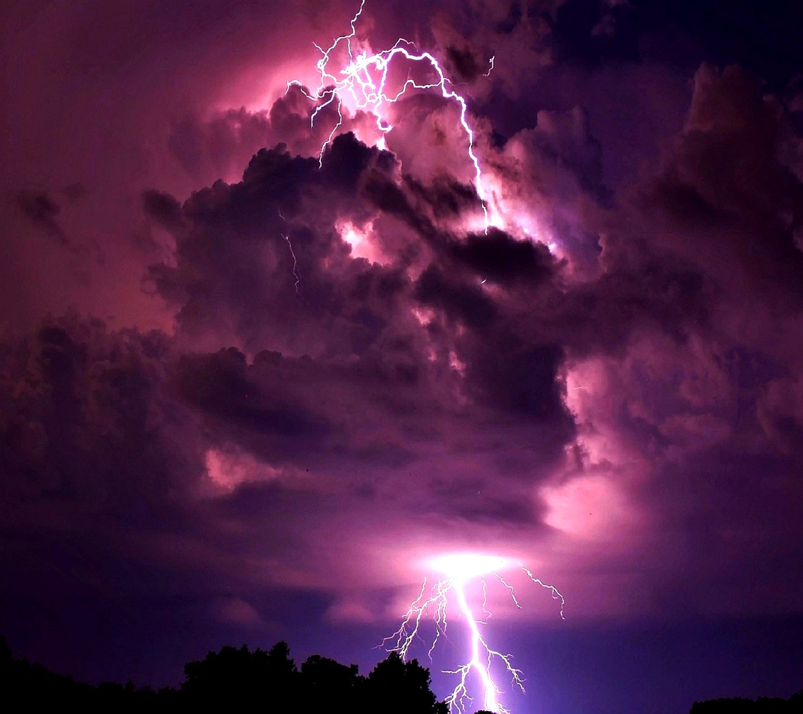 Lightning strikes through a dark purple sky with a person standing in the foreground (nature)