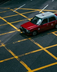 Taxi sedán rojo cruzando intersección marcada en amarillo en carretera de asfalto