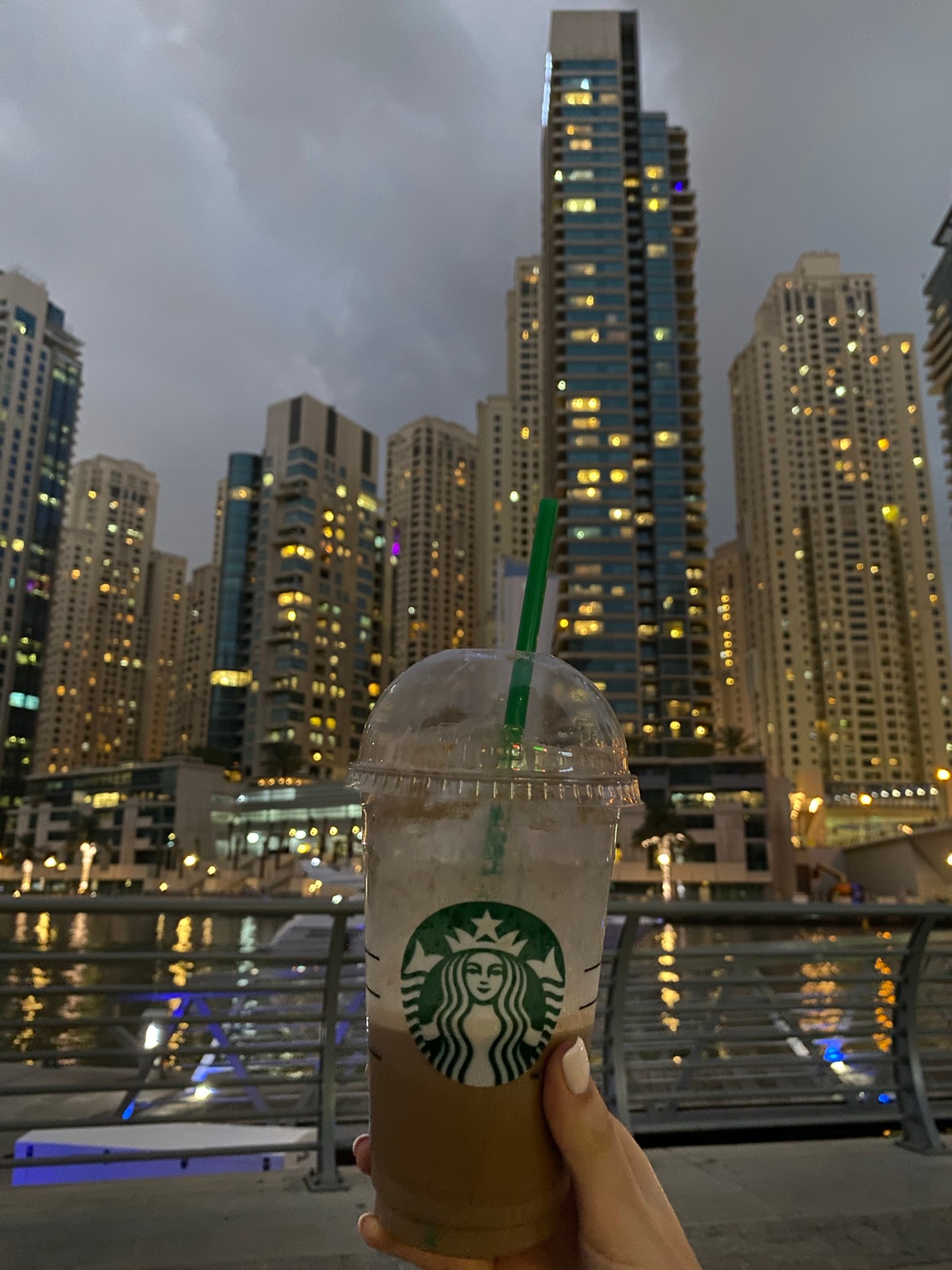 Напиток starbucks в пластиковом стакане с соломинкой перед городским пейзажем (башенный блок, метрополия, городская территория, городской пейзаж, город)