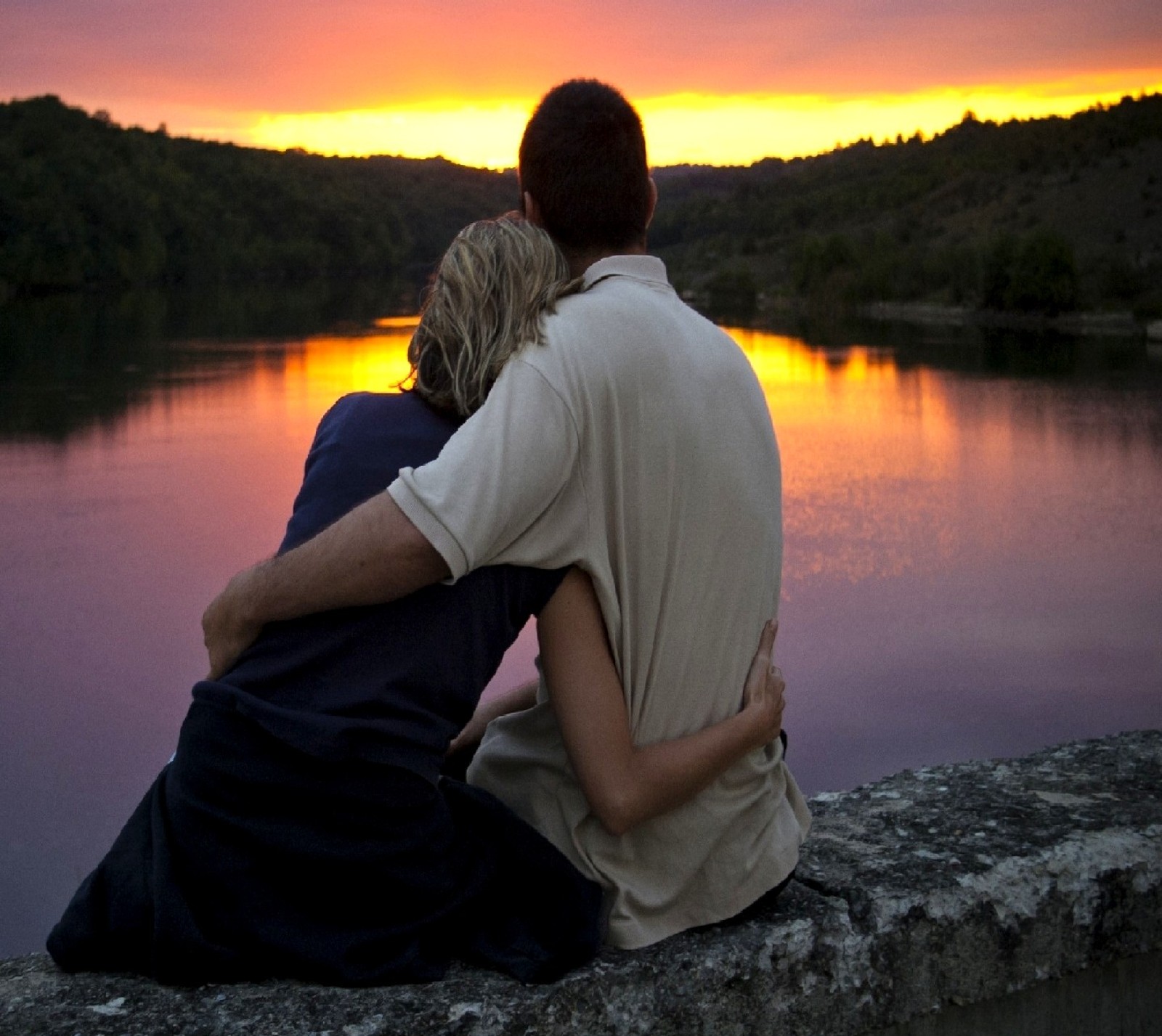 Deux personnes assises sur un mur regardent le coucher de soleil (amour)