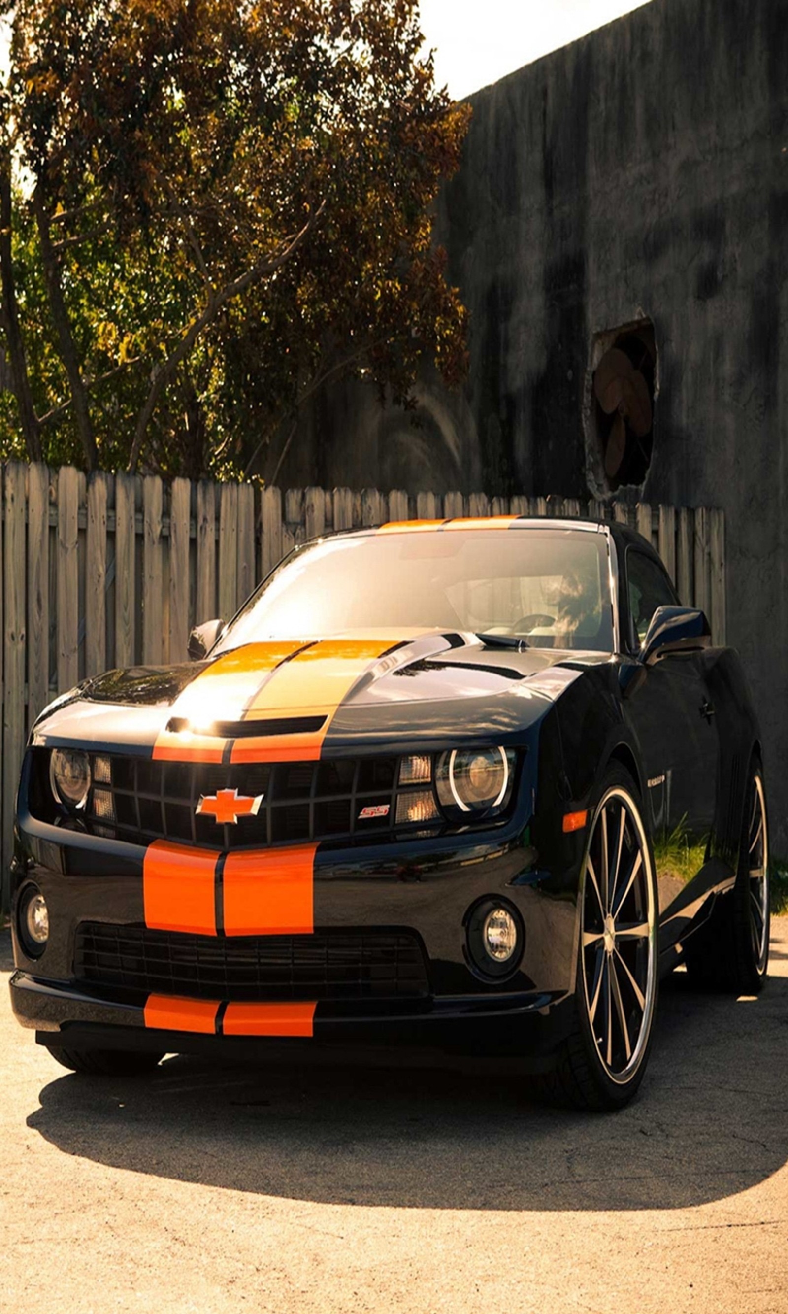 Arafed black car with orange stripes parked in front of a fence (camaro, car, classic, muscle, new)