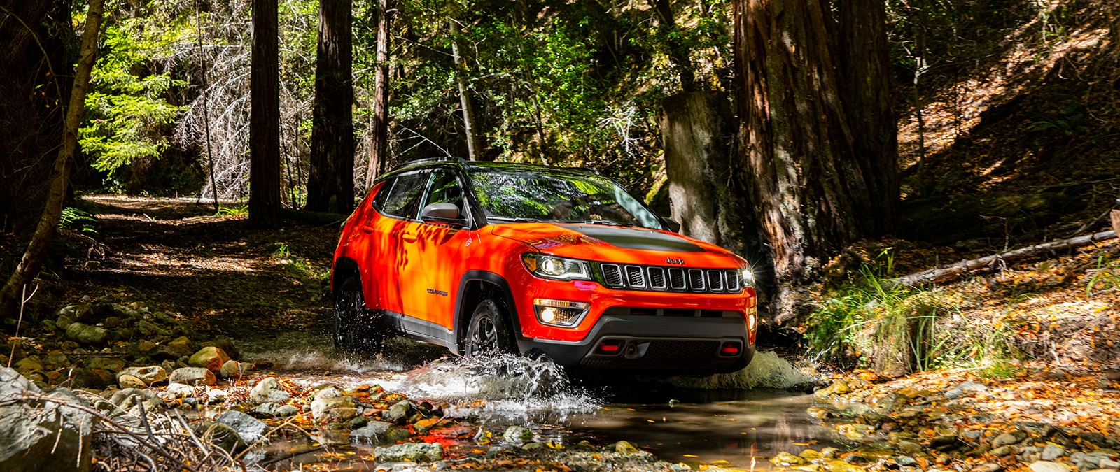 Um jipe vermelho atravessando um riacho na floresta (jeep, chrysler, carro, off road, planta)