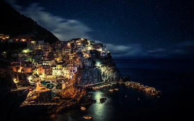 Manarola de noche: un impresionante paisaje marino bajo un cielo estrellado con barcos y efectos de larga exposición.