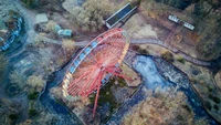 Vista aérea de uma roda-gigante colorida entre árvores nuas e um caminho sinuoso em Berlim.