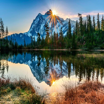 Majestätischer Sonnenaufgang über schneebedeckten Bergen, die sich in einem ruhigen See spiegeln.