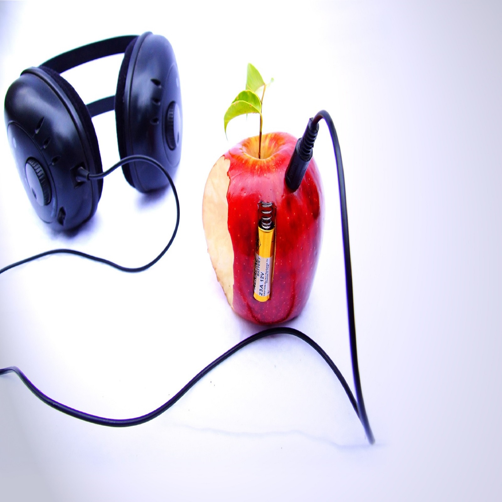 There is a red apple with a green leaf and headphones on (apple, ipod, music)