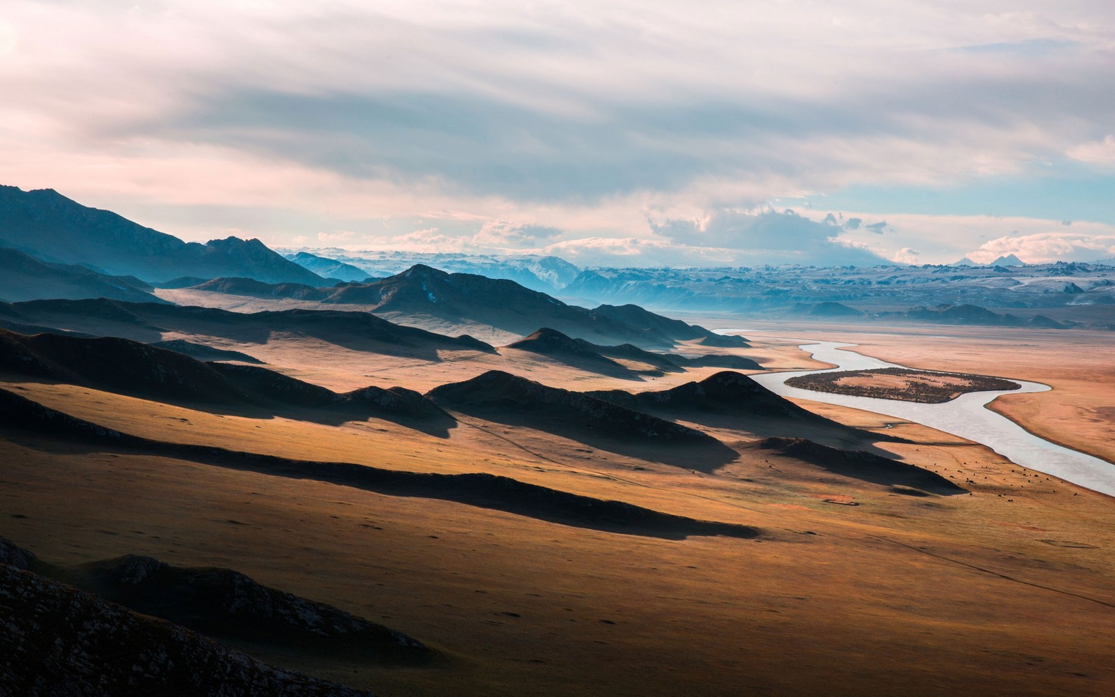 Une vue d'une rivière traversant une vallée au milieu d'un désert (formes montagneuses, nature, nuage, sauvage, hauts plateaux)