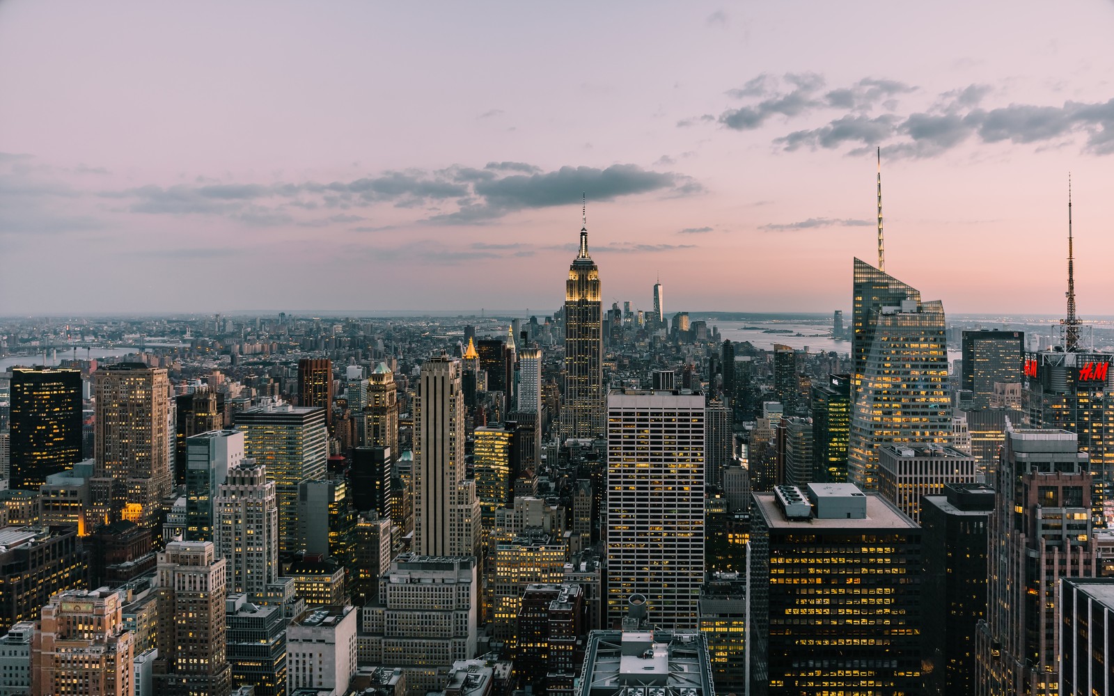 A view of a city skyline at dusk with skyscrapers and a red light (new york city, city, top of the rock, cloud, building)