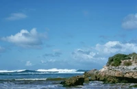 Waves crashing against rocky shorelines under a blue sky with scattered clouds at Kangaroo Island.