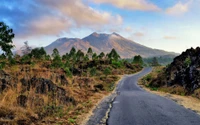 Scenic mountain landscape with a winding road, lush vegetation, and dramatic clouds.