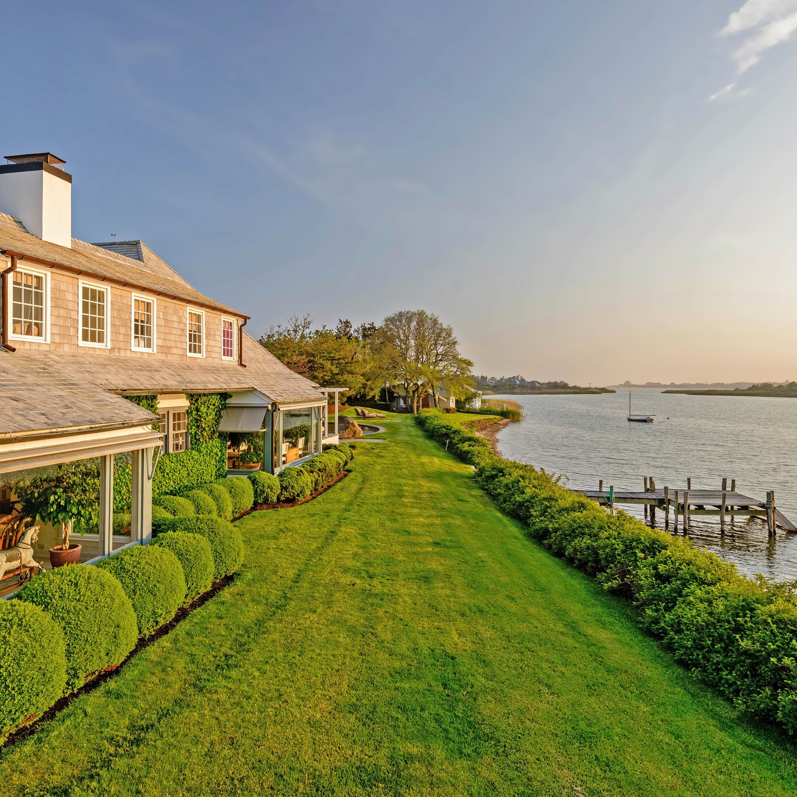 Uma vista de uma casa com um barco na água (hamptons, lar, casa, luxo, mar)