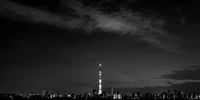 Monochrome Urban Skyline at Dusk with Tower Illuminated Against a Dramatic Cloudy Sky