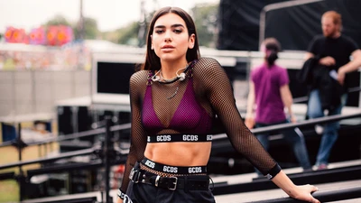 Dua Lipa in einem stylischen Netzoutfit an einem Konzertort.