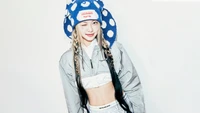 Eunchae en una pose juguetona, usando un elegante sombrero azul con lunares y un chic atuendo plateado, exudando energía juvenil y confianza.