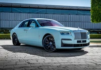 Elegant Rolls Royce Ghost in a striking light blue finish, showcasing its luxurious design against a modern architectural backdrop.