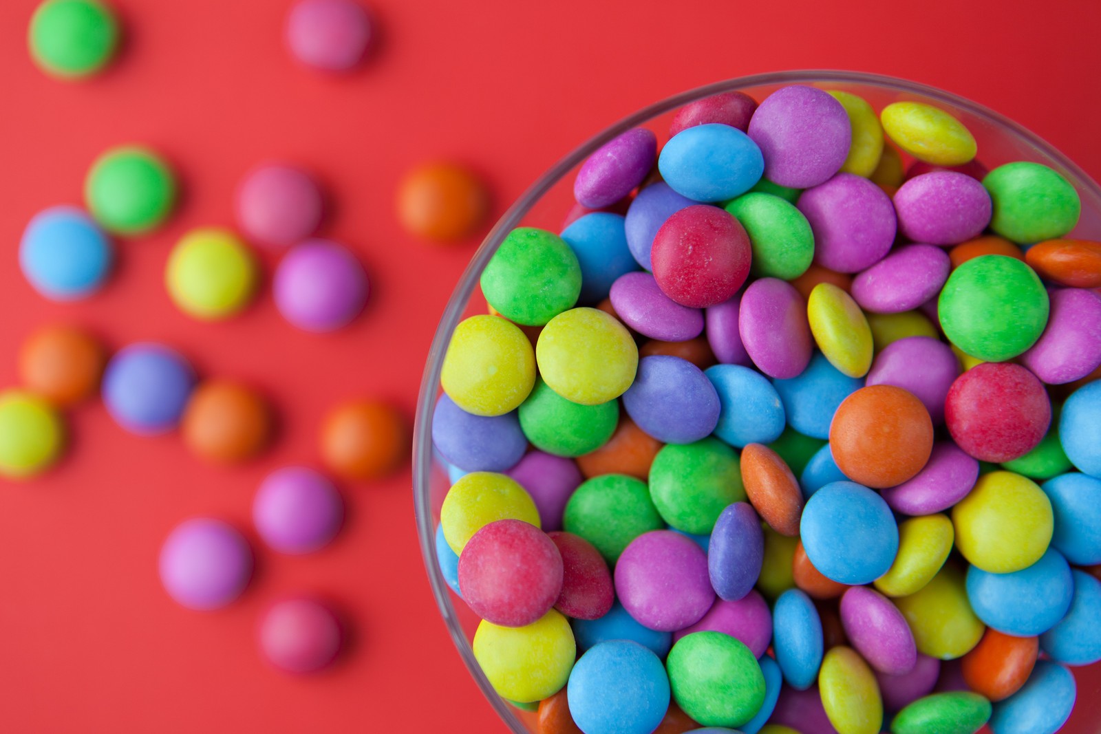 Un primer plano de un tazón de caramelos coloridos sobre una superficie roja (dulces, color, postre, dulzura, comida)