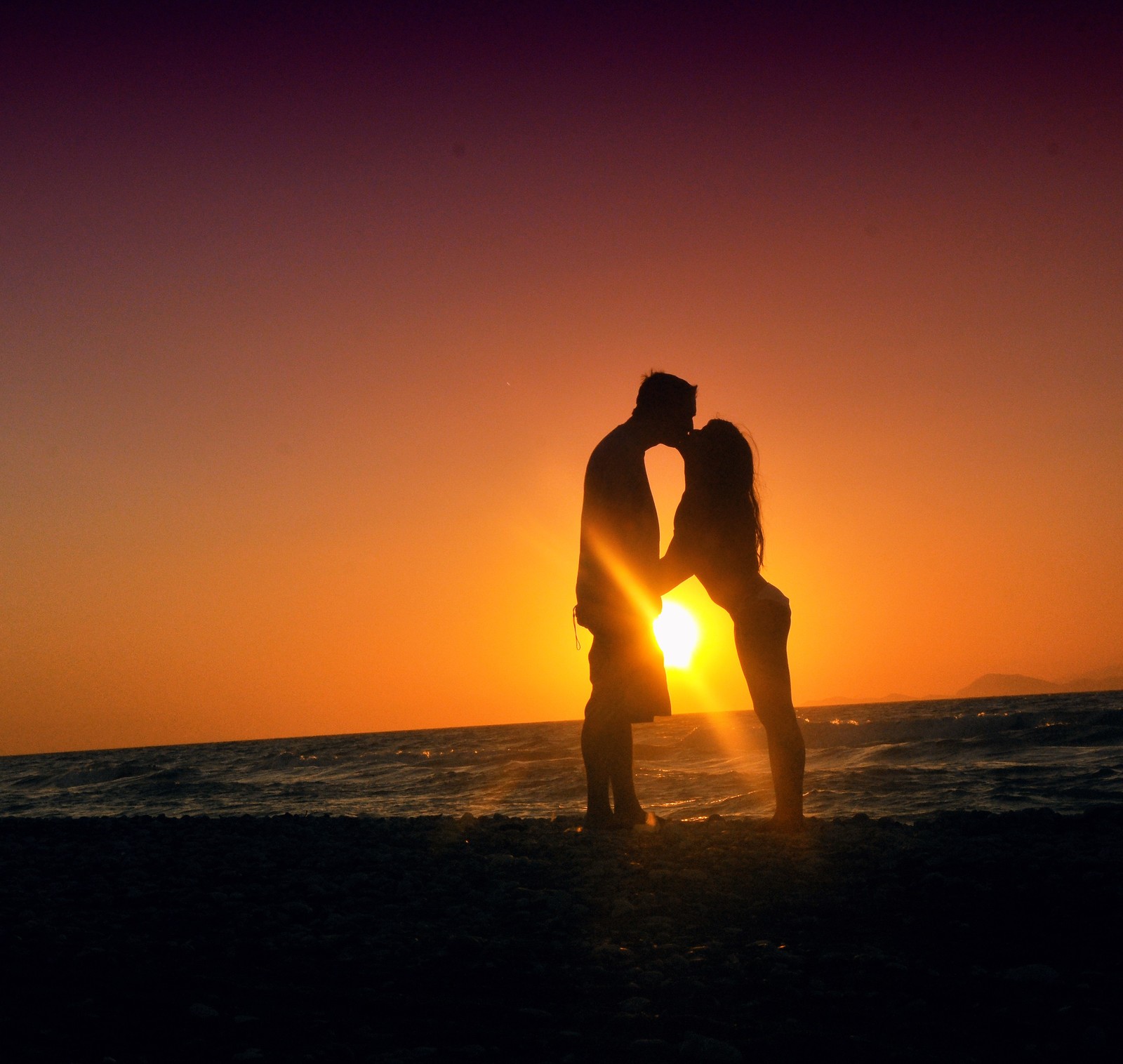 Duas pessoas estão em pé na praia ao pôr do sol (por do sol, pessoas na natureza, horizonte, amor, romance)