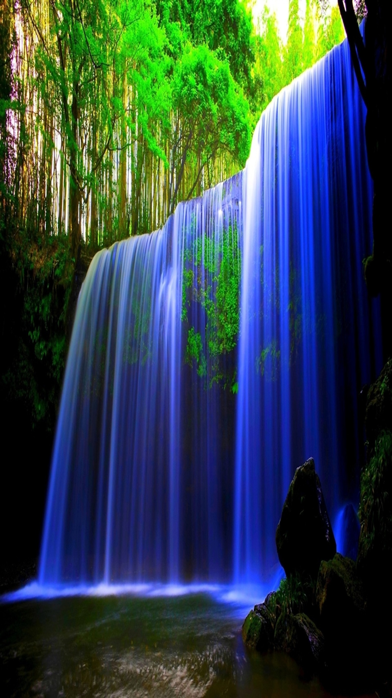 Un primer plano de una cascada con una persona sentada en una roca (azul, tranquilo, genial, bosque, verde)