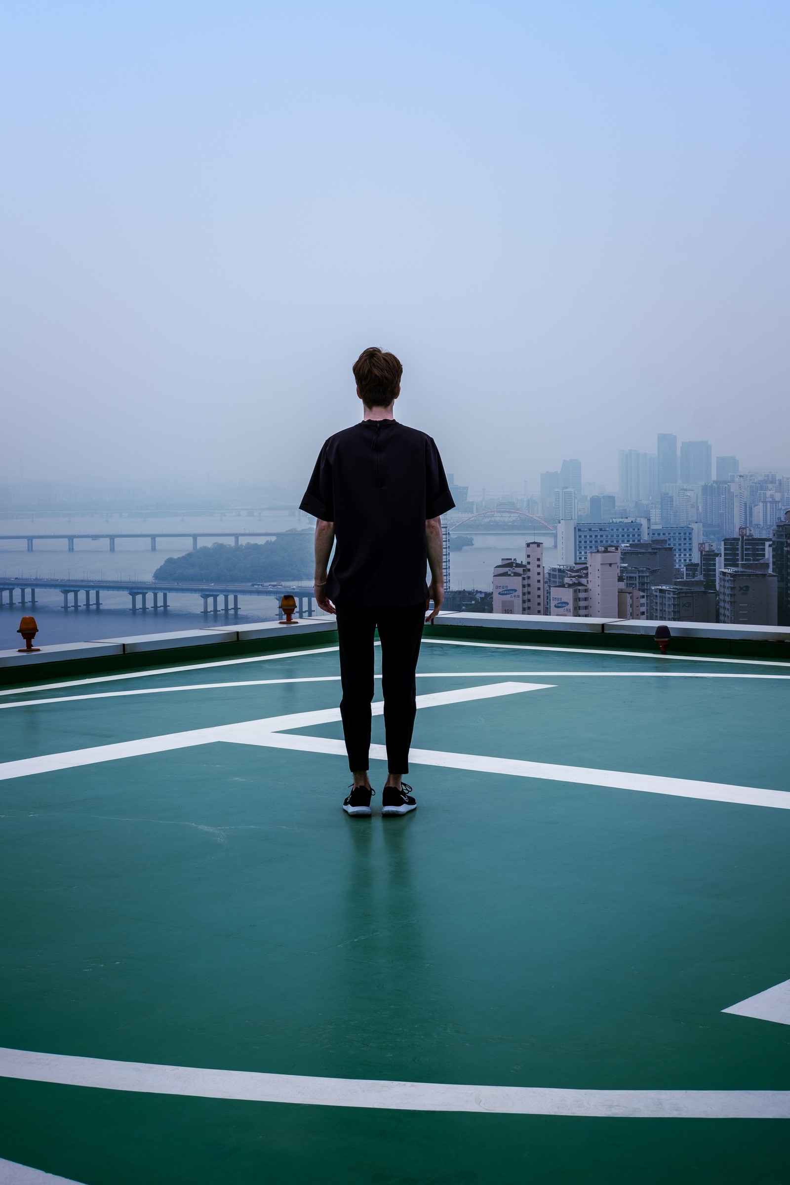 Un homme se tient sur un court de tennis avec une ville en arrière-plan (corée du sud, debout, architecture, ville, chaussures)