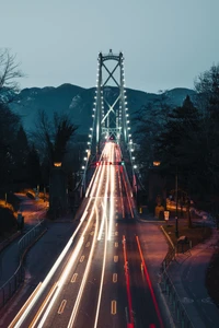 Pont suspendu illuminé la nuit avec des traînées de circulation et un arrière-plan montagneux