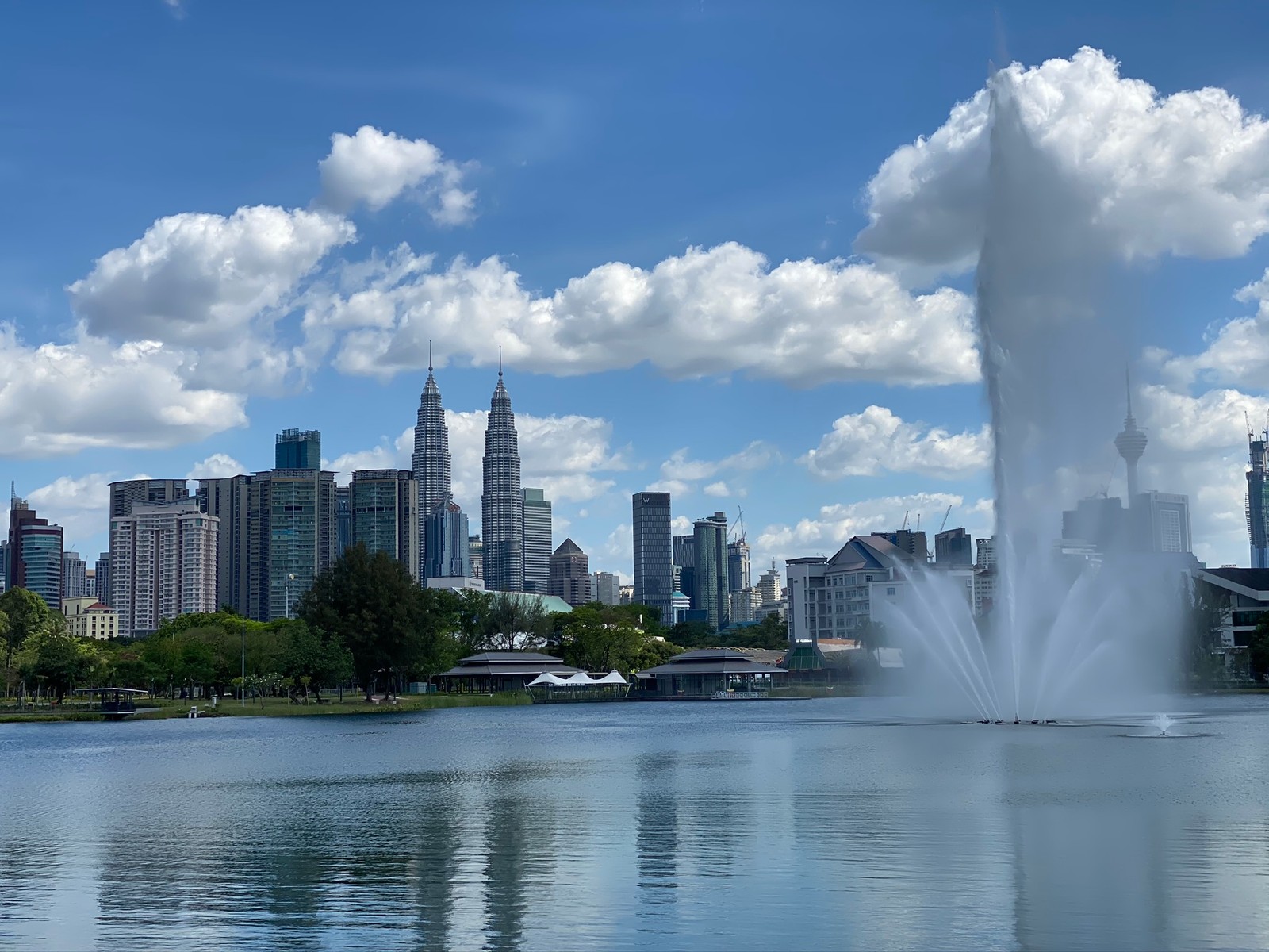 Uma fonte no meio de um lago com uma cidade ao fundo (torres petronas, kuala lumpur, linha do horizonte, corpo de água, fonte)