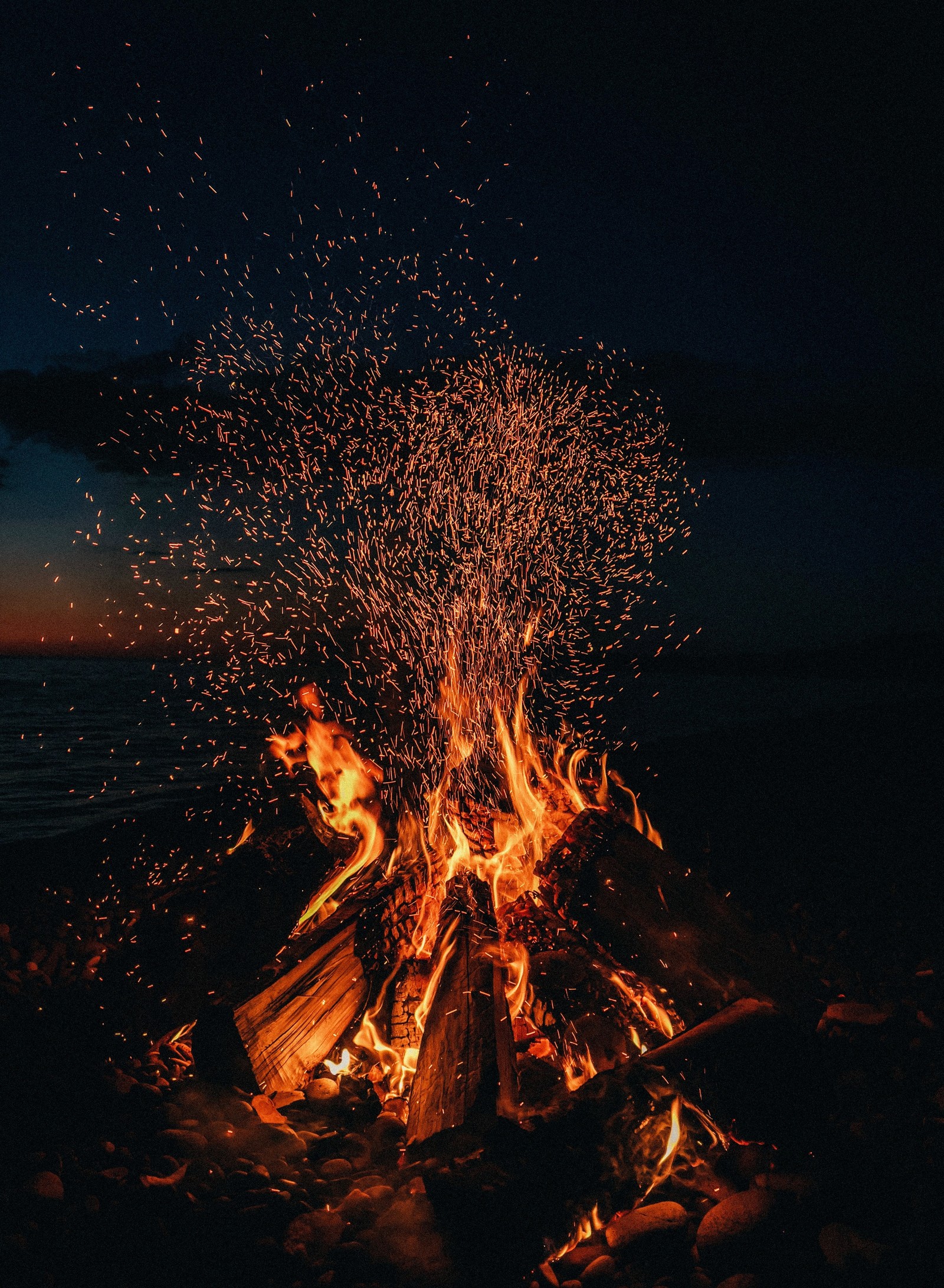 There is a fire that is burning in the sand by the water (bonfire, campfire, camping, heat, fire)