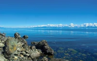 Rives tranquilles du lac Baïkal sous un ciel bleu clair, avec des côtes rocheuses et des eaux sereines.