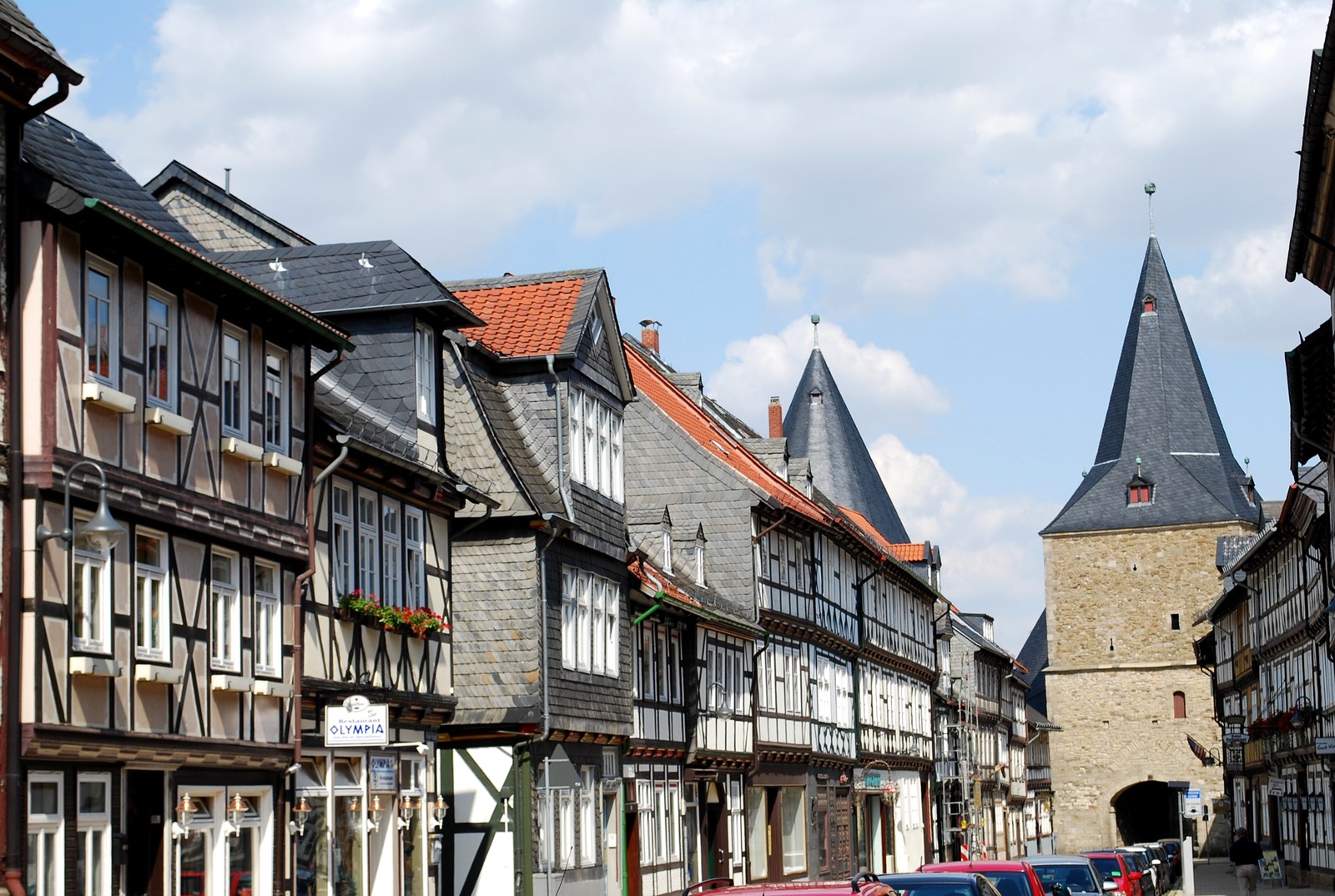 Cars parked on the side of the road in front of a row of buildings (building, medieval architecture, town, neighbourhood, street)