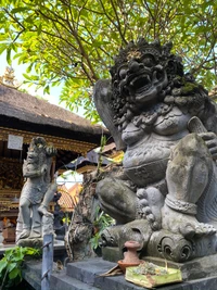 Majestätische steinerne Wächterstatuen an einem balinesischen Tempel, umgeben von üppigem Grün, mit kunstvollen Schnitzereien und antiker Kunstfertigkeit.