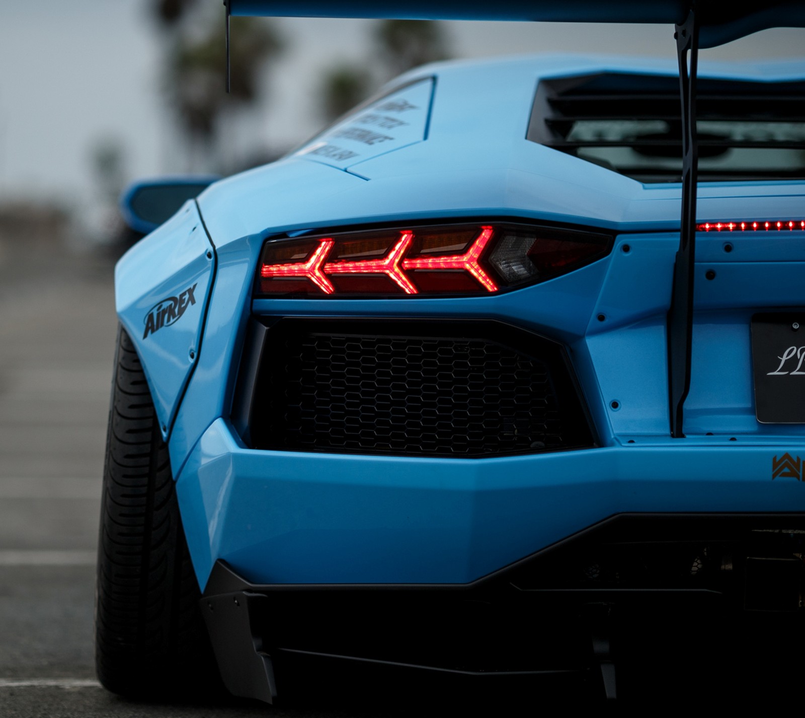 A close up of a blue sports car parked in a parking lot (blue, car, eye, lamborghini)