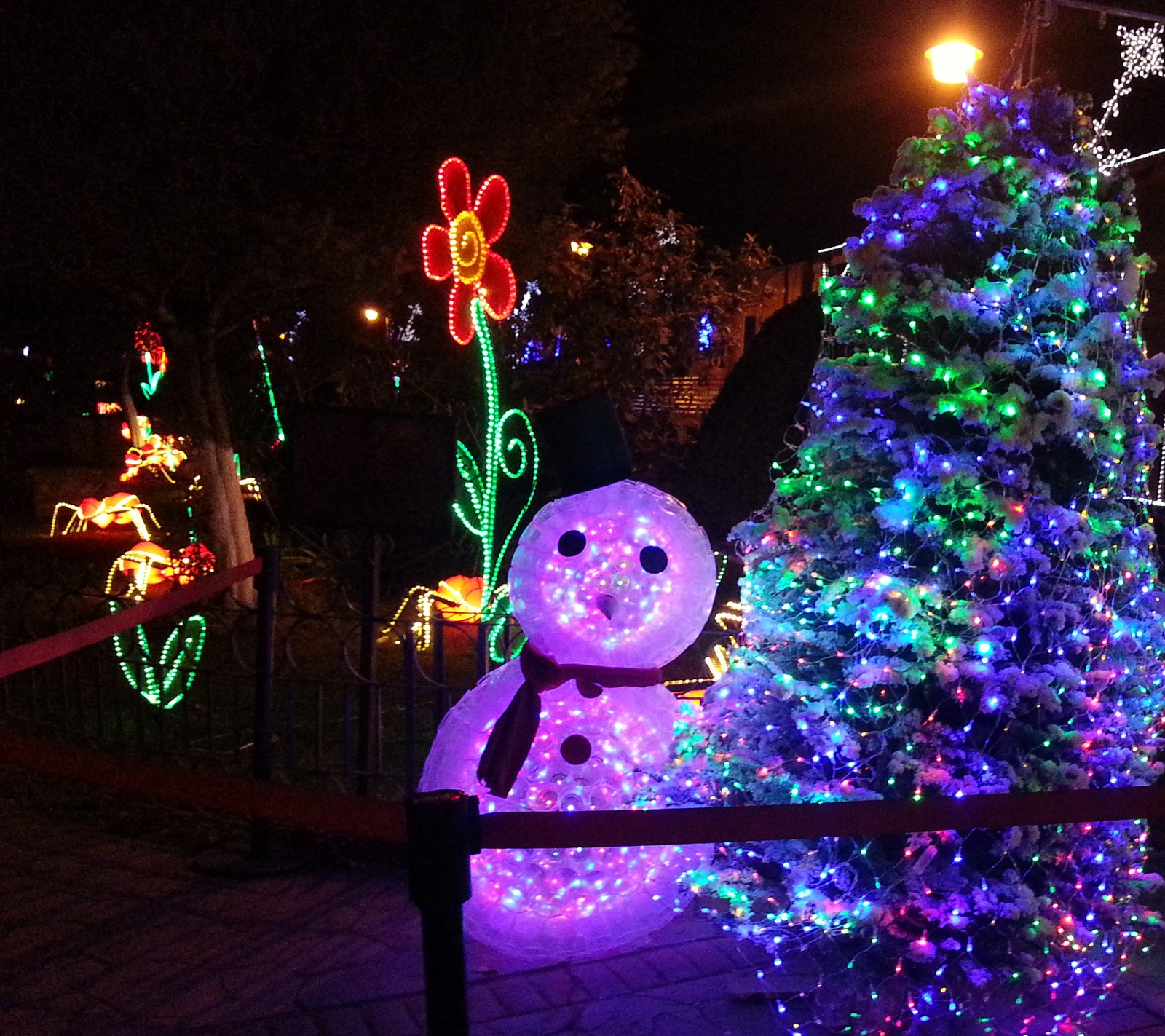 Árbol de navidad con luces y un muñeco de nieve frente a una cerca (diciembre, navidad)