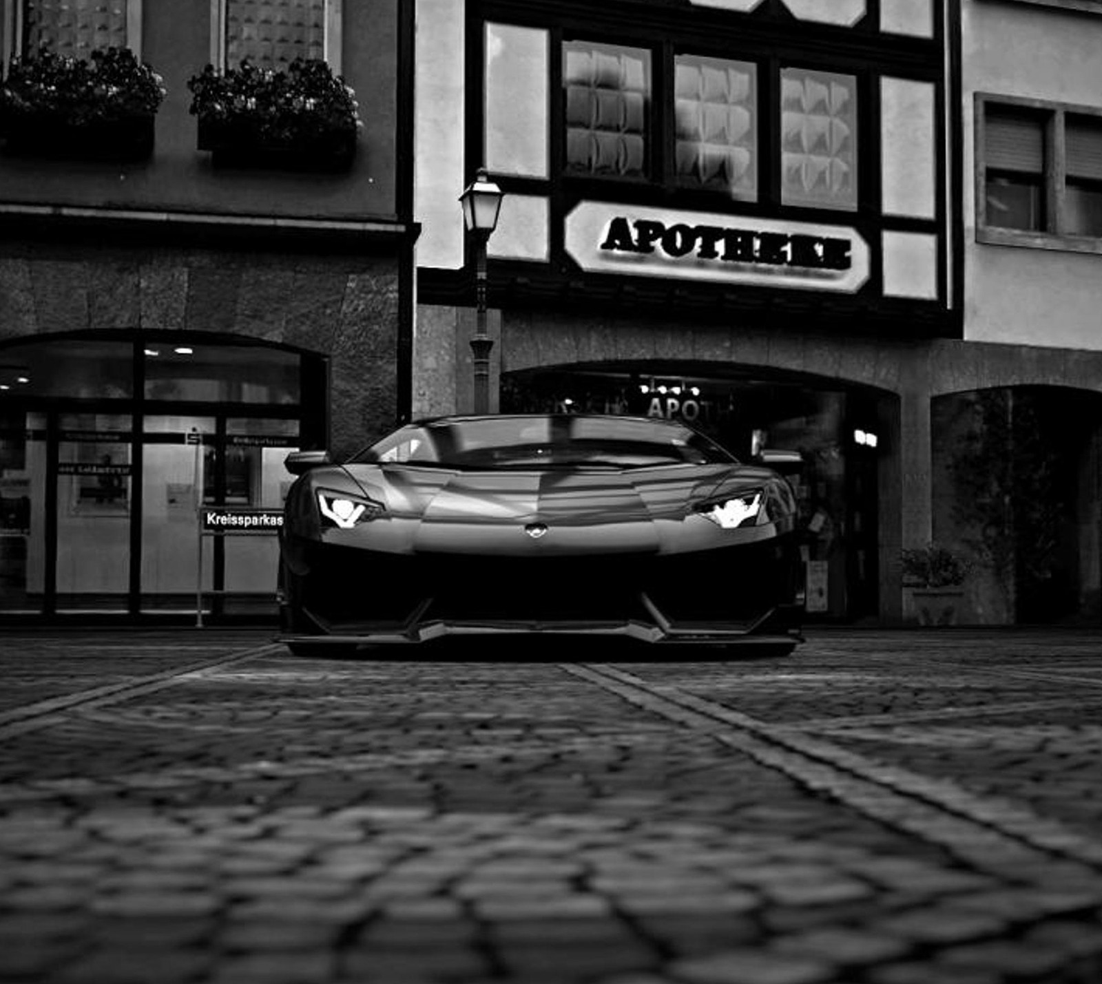 A black and white photo of a sports car parked in front of a building (auto, dark car, lamborghini)