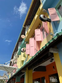 Colorful storefronts with vibrant shutters and a balcony under a clear blue sky.