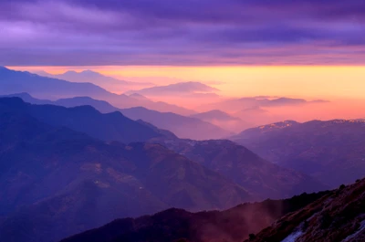 Cadena montañosa neblinosa al atardecer con cielo púrpura