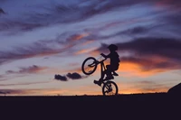 Silhouette d'un cycliste effectuant un wheeling contre un ciel de coucher de soleil vibrant.