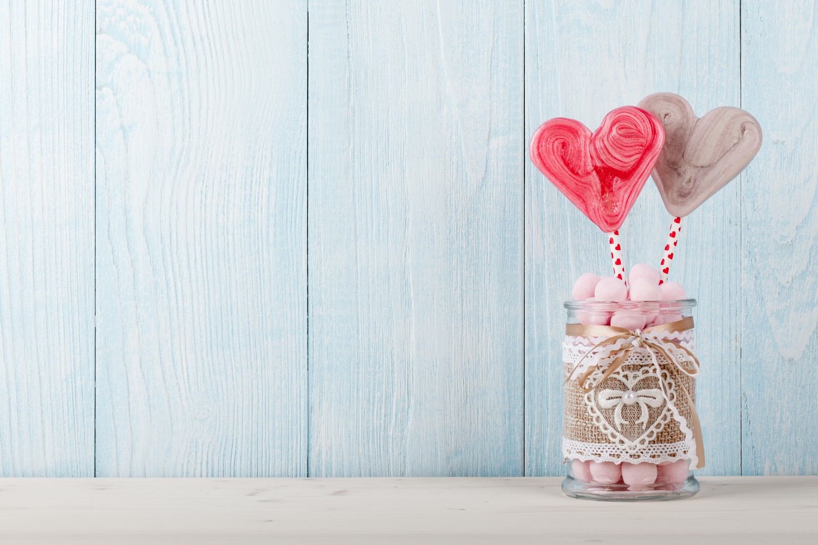 Il y a deux sucettes en forme de cœur dans un bocal sur une table (cœur, romance, rose, amour, douceur)