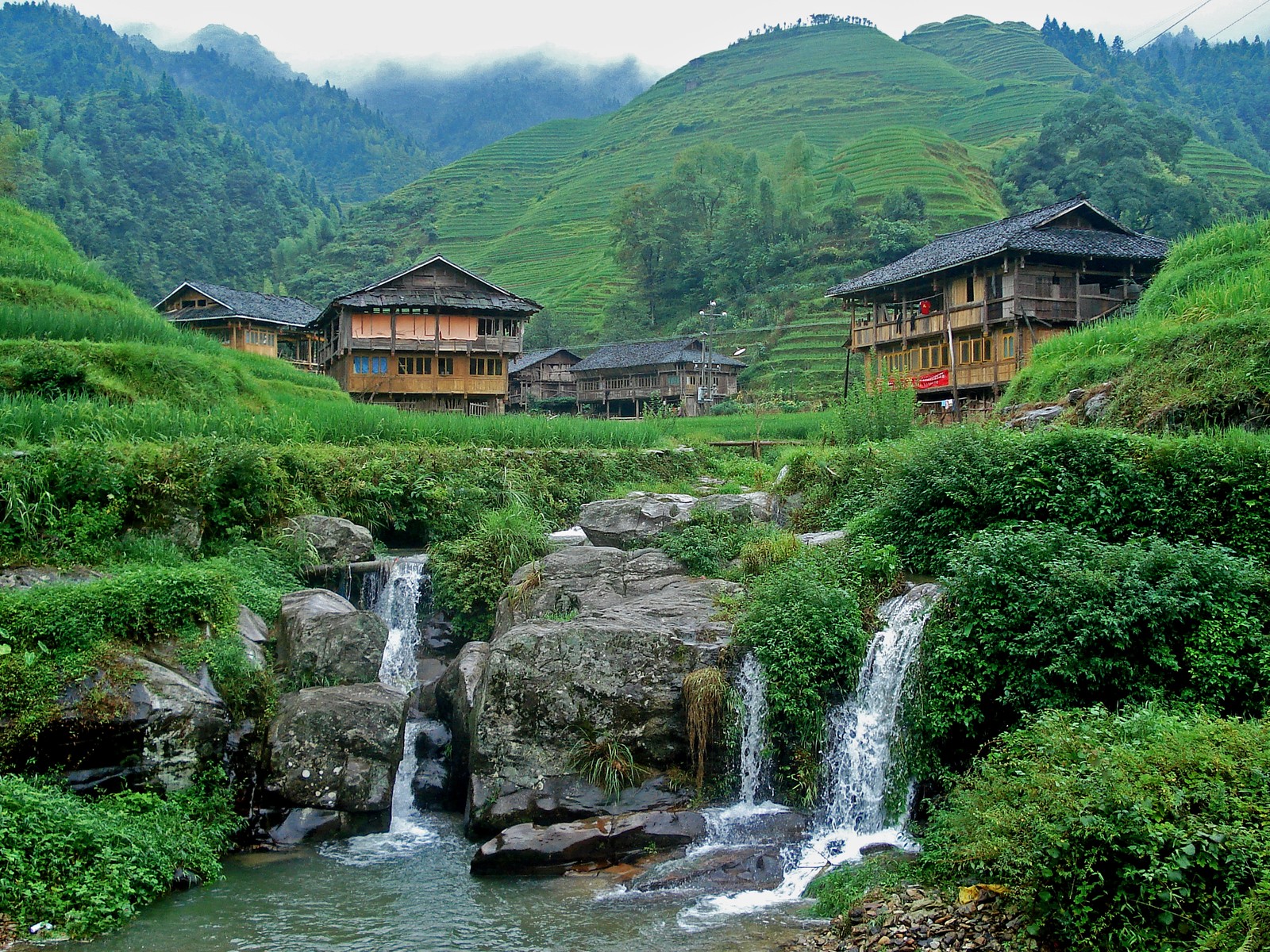 Há muitas casas na encosta da montanha com uma cachoeira (recursos hídricos, natureza, água, estação de montanha, aldeia montanhosa)